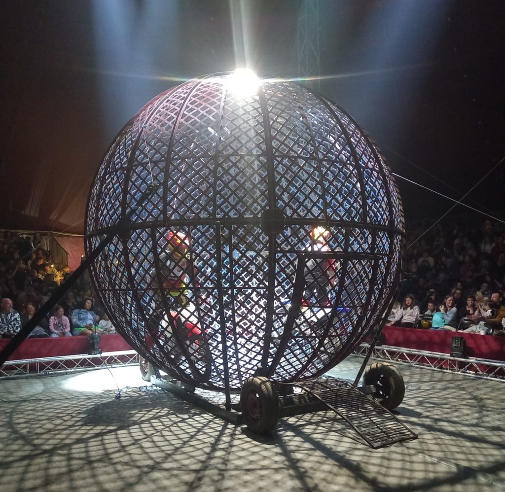A photo of a giant metal ball with motorcycles in it in the middle of a big stage.